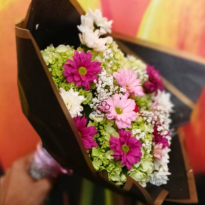 Mother's Day bouquet bursting with bright pink, white, and fuchsia chrysanthemums and daisies, wrapped stylishly in black paper.