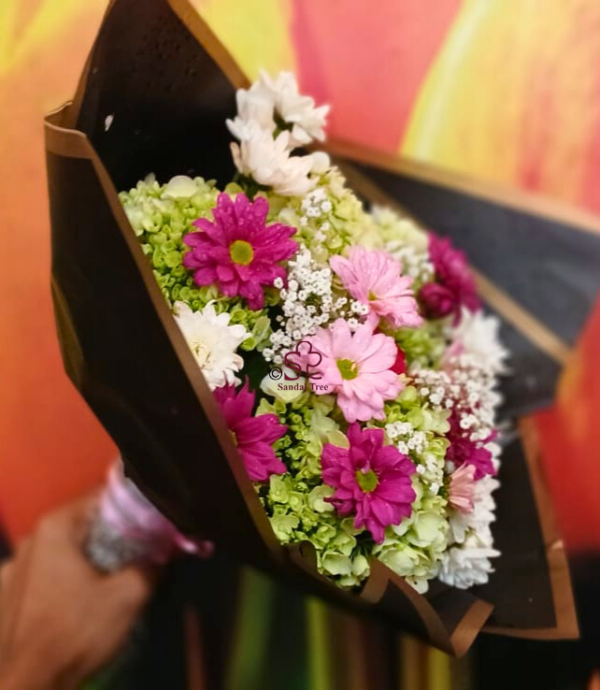 Mother's Day bouquet bursting with bright pink, white, and fuchsia chrysanthemums and daisies, wrapped stylishly in black paper.